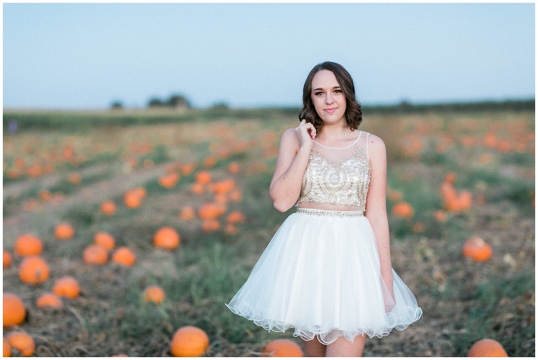 girl in a white prom dress standing in a pumpkin patch